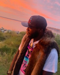 a man in a fur vest standing in front of the ocean